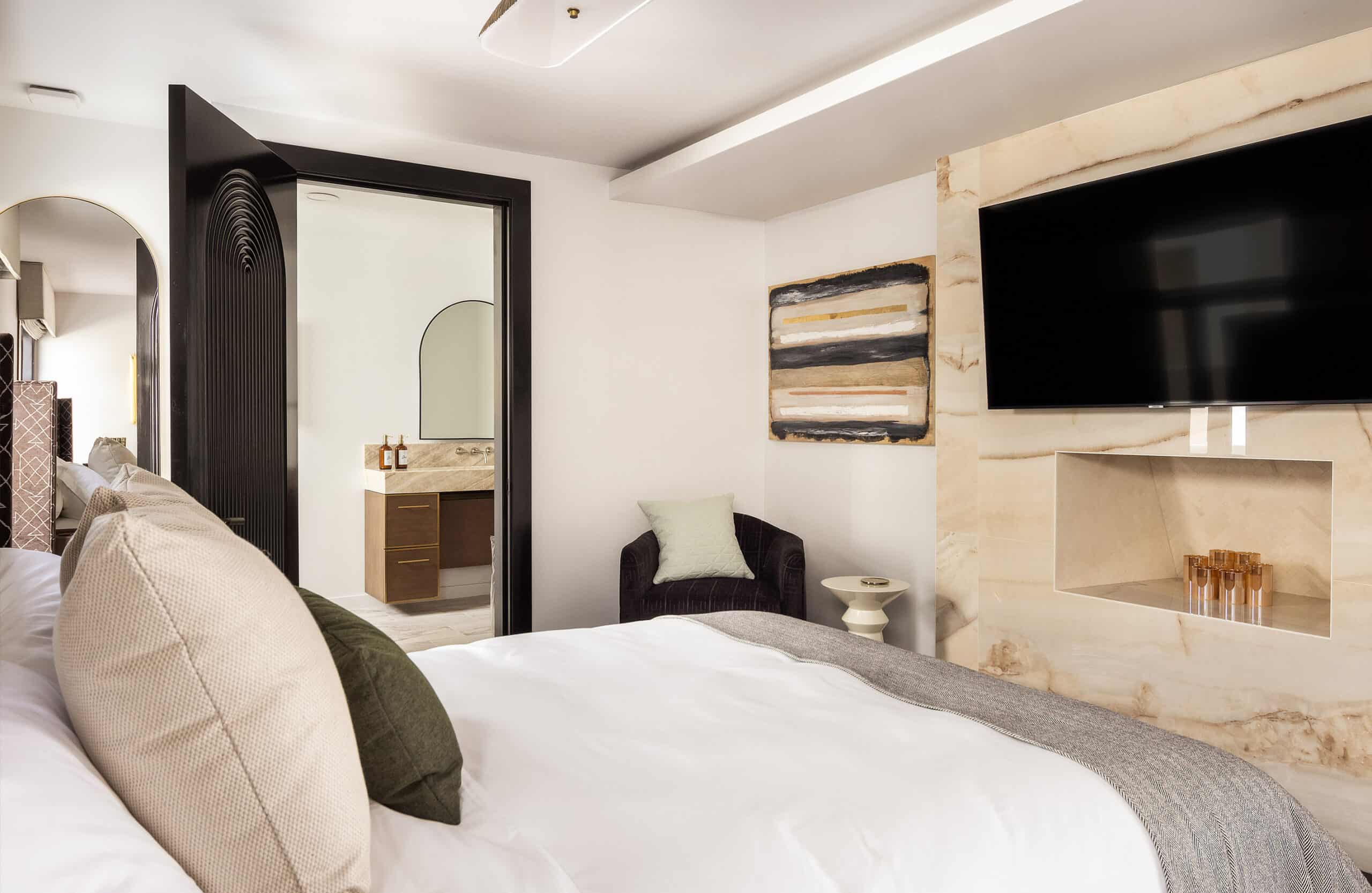 Contemporary bedroom featuring marble accent wall, wall-mounted television, and open view into modern bathroom.