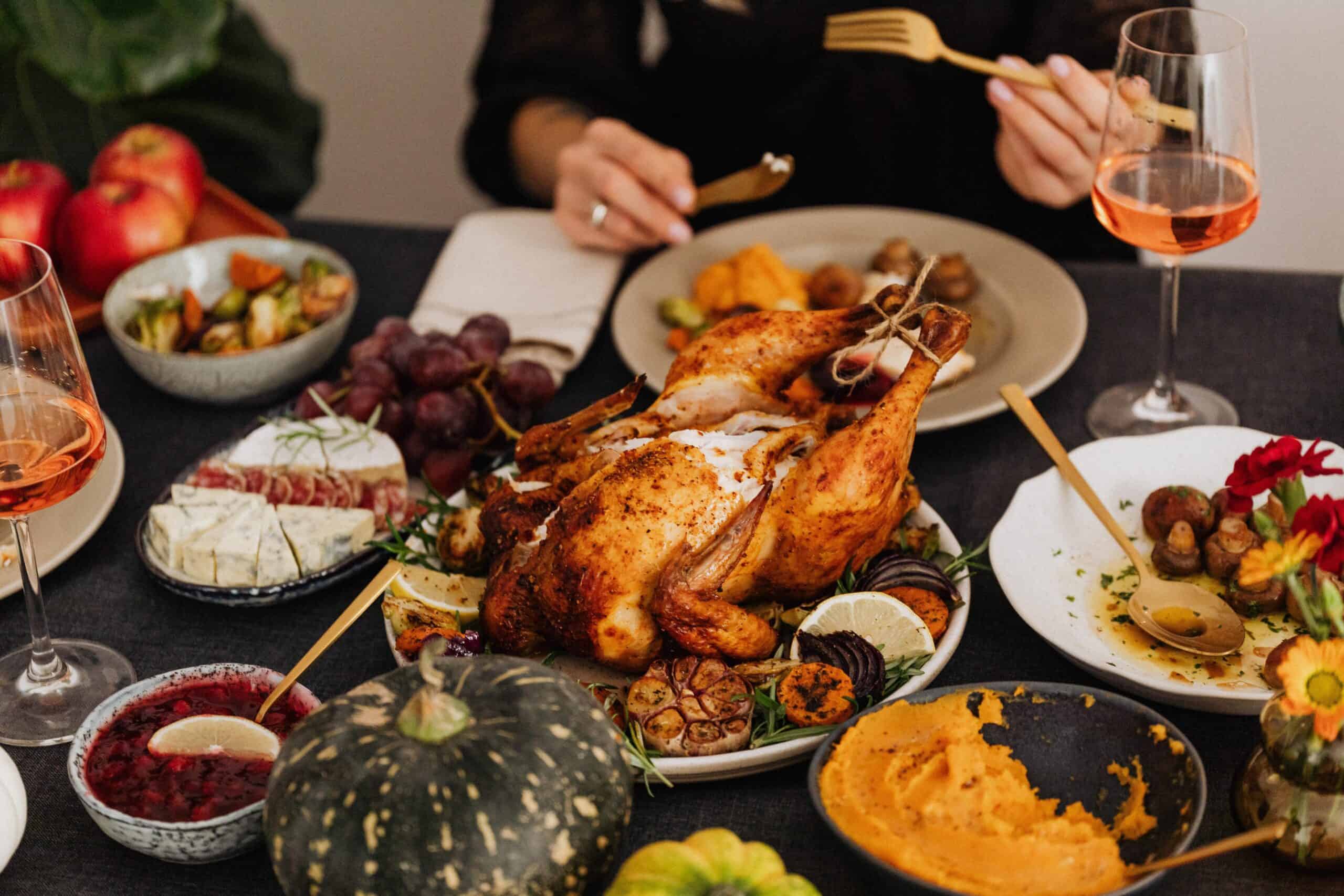 Festive dinner table featuring a whole roasted chicken surrounded by seasonal sides, wine glasses, and autumn decor.
