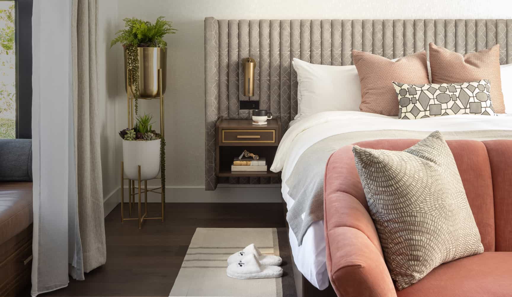 Luxury hotel bedroom with upholstered bed, blush accent sofa, layered pillows, and elegant bedside décor