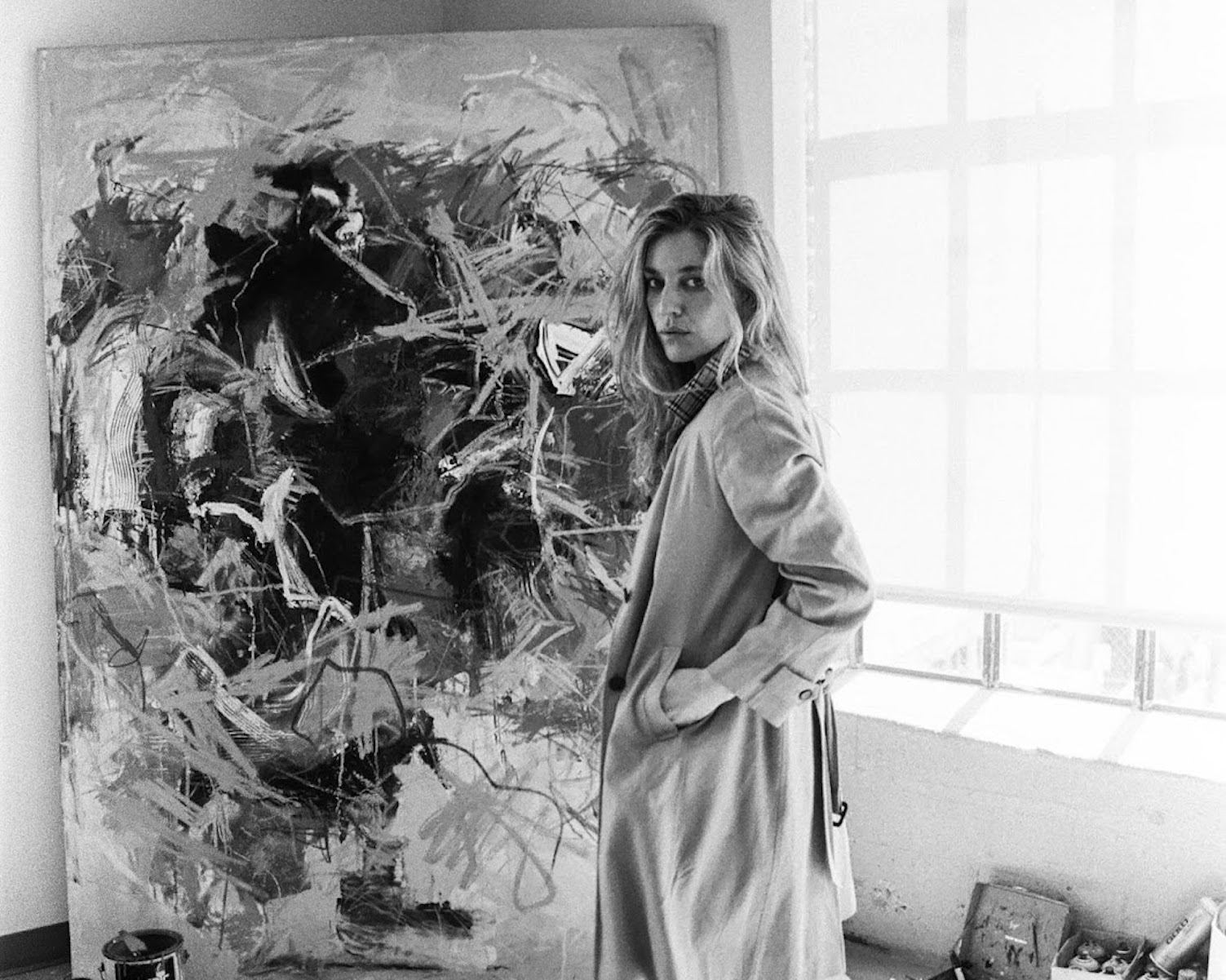 “Female artist posing next to an expressive abstract painting in a minimalist studio space.