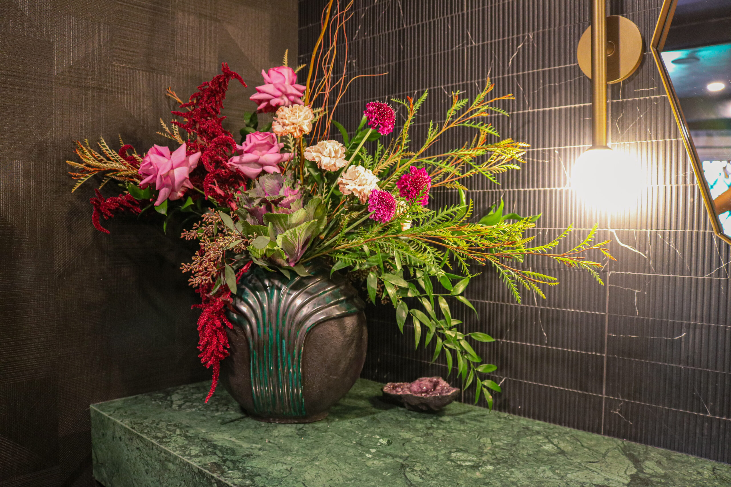 Elegant floral arrangement in a decorative vase placed on a green marble surface with warm ambient lighting in a modern interior