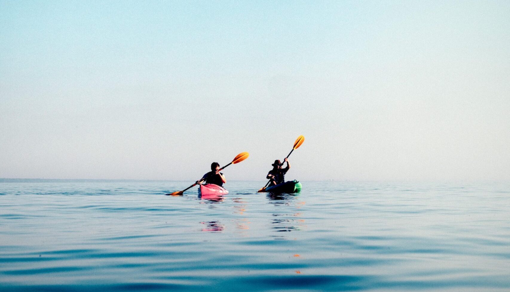 Two people kayaking together on calm ocean water under a clear sky during a peaceful coastal outing