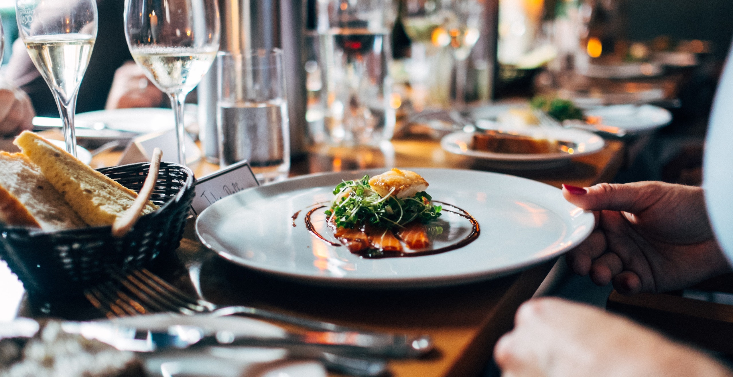Elegant plated fine-dining dish being served at a restaurant table set with wine glasses and gourmet tableware