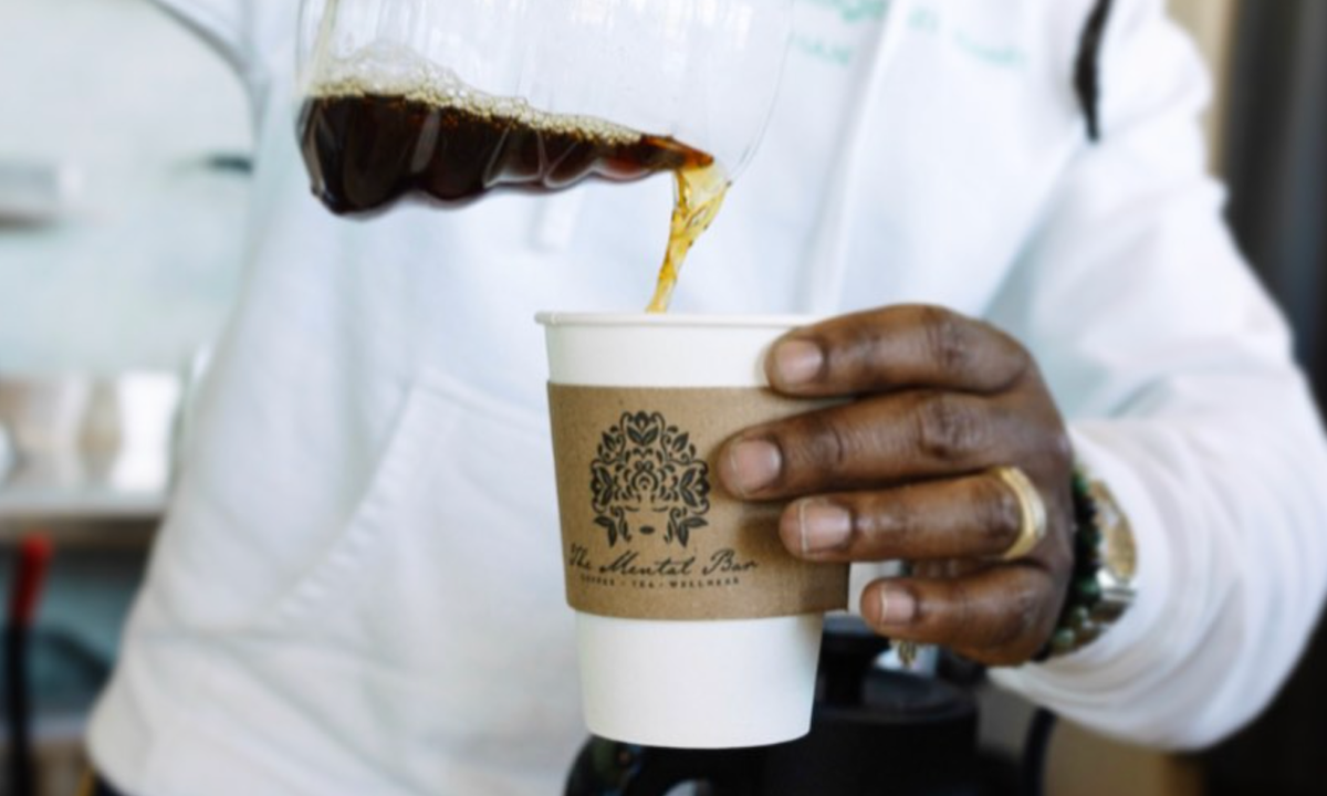 Freshly brewed coffee being poured from a glass carafe into a branded takeaway cup by a barista