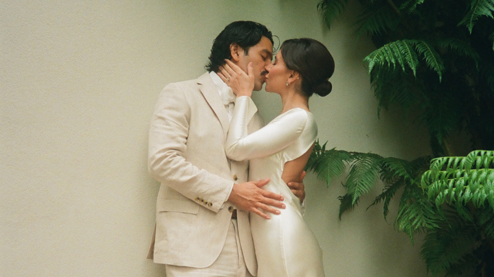 Bride and groom sharing a romantic kiss in an intimate outdoor setting surrounded by greenery