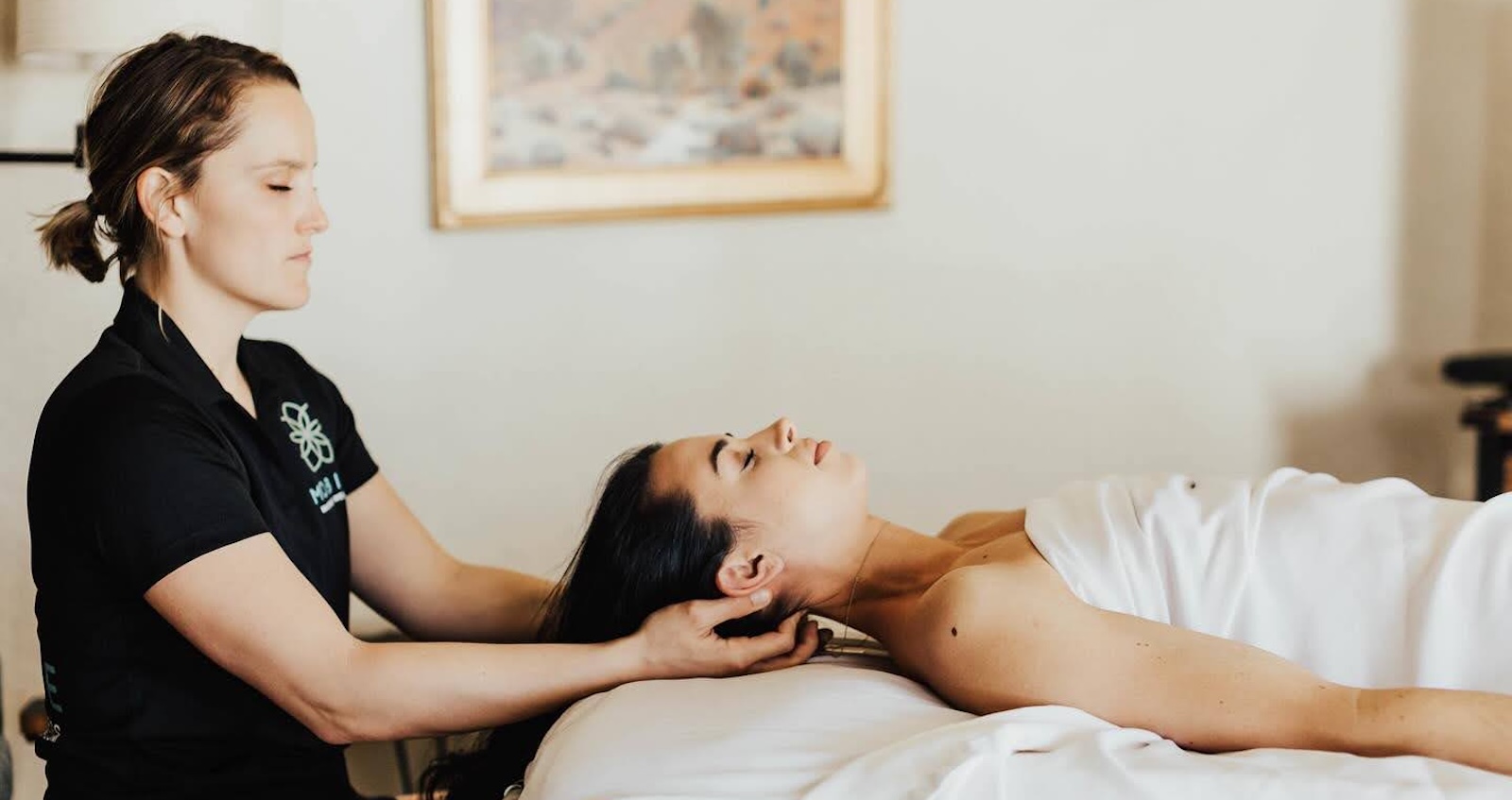 Spa therapist performing a relaxing head and neck massage on a woman lying on a treatment table in a serene wellness setting