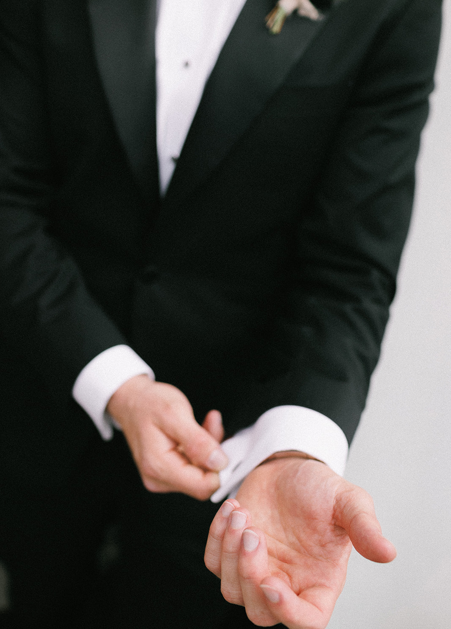 Groom adjusting his cufflinks while wearing a black tuxedo during wedding preparations.
