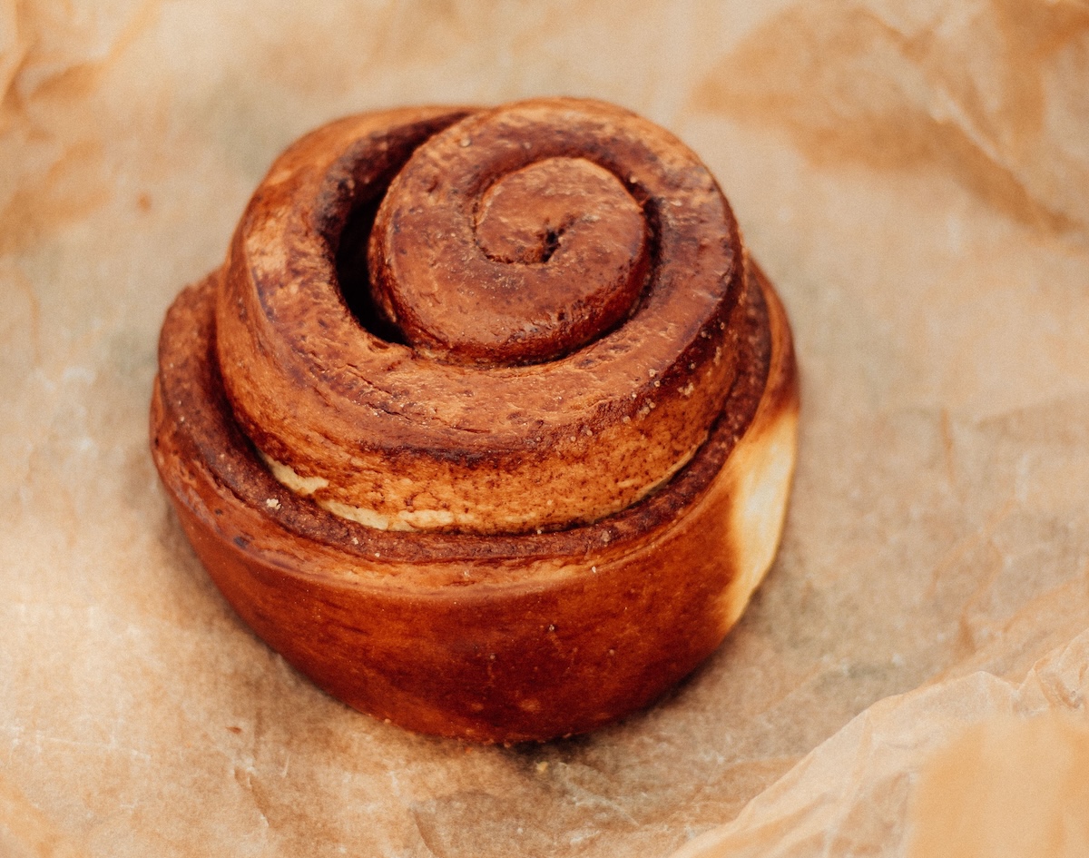 Close-up of a freshly baked cinnamon roll with a golden-brown spiral, resting on crinkled parchment paper.