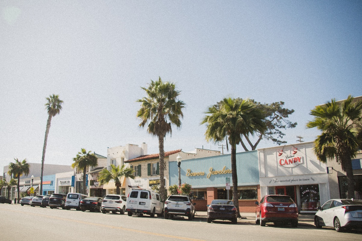 ORLI JDNPHOTOGRAPHY(22of35) Palm-lined neighborhood street with local storefronts and parked cars on a sunny day.