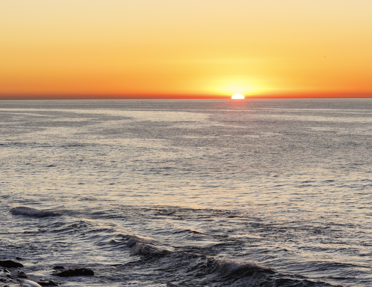 Orli 2024 Medres Will Edwards 109 Sun setting over the ocean, casting a warm orange glow across the sky and gentle waves.