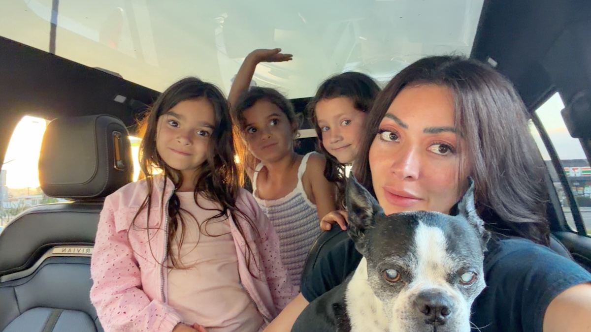 image6 Woman taking a selfie with three children and a black-and-white dog inside a car.
